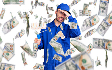 Young hispanic man wearing painter uniform holding roller stressed and frustrated with hand on head, surprised and angry face