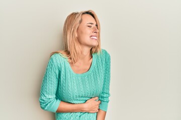 Obraz premium Beautiful blonde woman wearing casual winter sweater with hand on stomach because nausea, painful disease feeling unwell. ache concept.