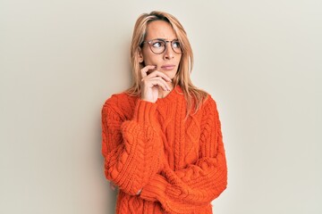Beautiful blonde woman wearing casual clothes and glasses thinking concentrated about doubt with...