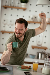 Handsome man preparing breakfast at home. Young man drinking coffee while preparing sandwich.