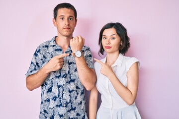 Beautiful couple wearing casual clothes in hurry pointing to watch time, impatience, looking at the...