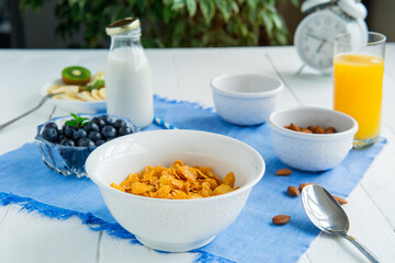 Nutritious healthy breakfast. Bowl with cereals, almonds, blueberry, plant-based milk, and orange fresh juice on a blue napkin and white wooden table. Day diet planning and healthy eating concept.
