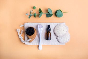 Home self-care kit for face massage. Dry lymphatic drainage brush, derma mezoroller, loofah pads, natural oil serum and eucalyptus on beige background. DIY natural eco cosmetics and home spa. Top view