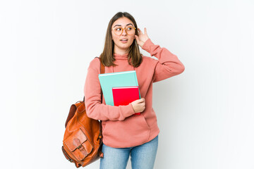 Young student woman isolated on white bakcground trying to listening a gossip.