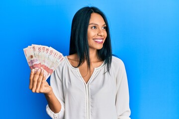 Young african american woman holding 10 colombian pesos banknotes looking away to side with smile on face, natural expression. laughing confident.