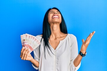 Young african american woman holding 10 colombian pesos banknotes crazy and mad shouting and yelling with aggressive expression and arms raised. frustration concept.