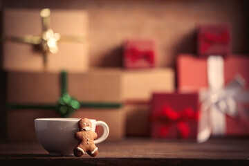 Cup of coffee with gingerbread man and Christmas gift on wooden table