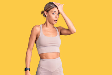 Beautiful caucasian woman wearing sportswear surprised with hand on head for mistake, remember...