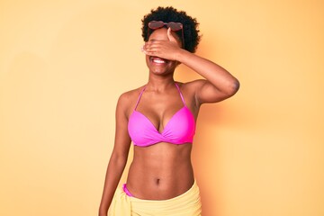 Young african american woman wearing bikini smiling and laughing with hand on face covering eyes for surprise. blind concept.