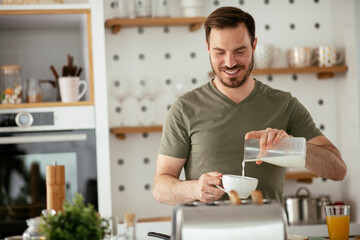 Handsome man preparing breakfast at home. Young man drinking coffee while preparing sandwich.