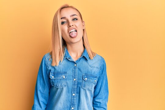 Beautiful caucasian woman wearing casual denim jacket sticking tongue out happy with funny expression. emotion concept.