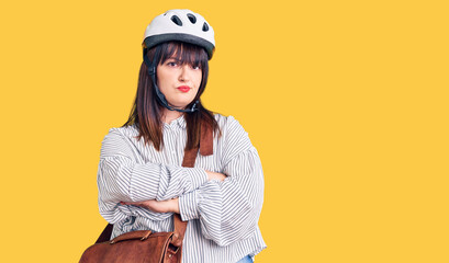 Young plus size woman wearing bike helmet and leather bag skeptic and nervous, disapproving expression on face with crossed arms. negative person.