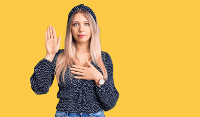 Young beautiful blonde woman wearing casual clothes swearing with hand on chest and open palm,...