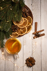 
a cup of hot Christmas tea with lemon on a light wood. against the background of an asterisk star anise, an orange and a sprig of a Christmas tree. christmas concept