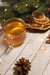 
a cup of hot Christmas tea with lemon on a light wood. against the background of an asterisk star anise, an orange and a sprig of a Christmas tree. christmas concept
