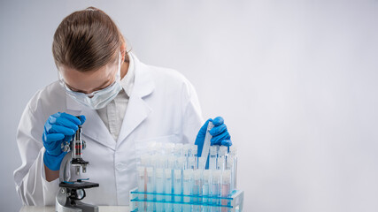 Microbiologists with PPE suit and face mask hold test tube and use microscope in lab, finding...