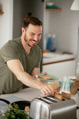 Handsome man preparing breakfast at home. Young man drinking coffee while preparing sandwich.