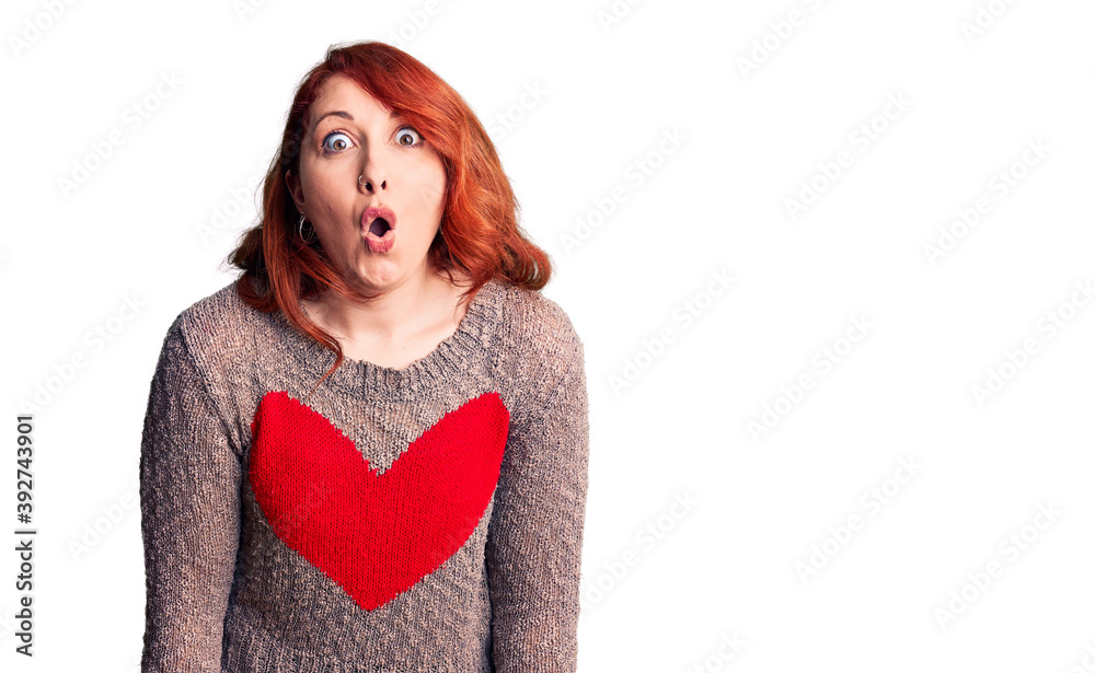 Poster Young beautiful redhead woman wearing casual heart sweater scared and amazed with open mouth for surprise, disbelief face