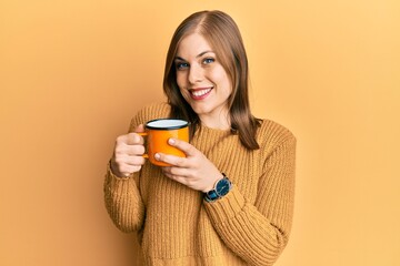 Beautiful caucasian woman drinking a cup coffee looking positive and happy standing and smiling with a confident smile showing teeth