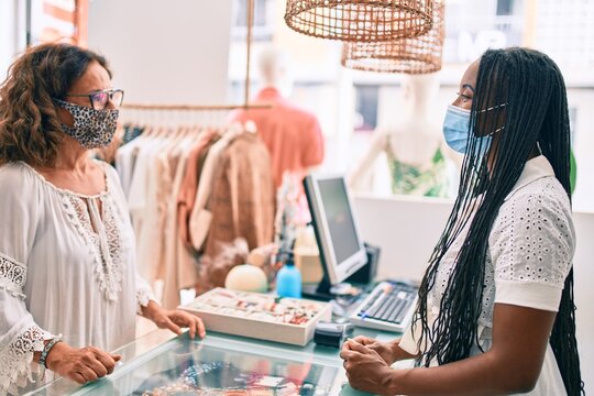 Young african american shopkeeper woman wearing medical mask working at clothing store