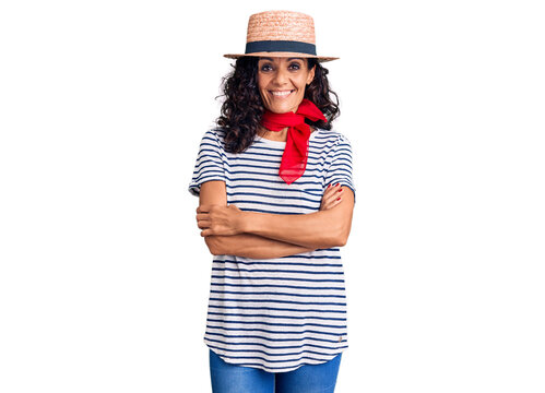 Middle age beautiful woman wearing casual striped t shirt and summer hat happy face smiling with crossed arms looking at the camera. positive person.