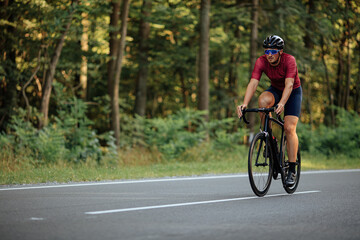 Fototapeta na wymiar Muscular guy in helmet riding bike on asphalt road