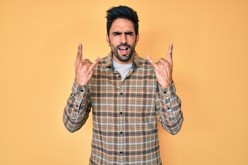 Handsome hispanic man with beard wearing casual clothes shouting with crazy expression doing rock symbol with hands up. music star. heavy concept.