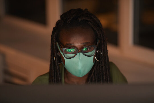 High Angle Portrait Of Contemporary African-American Woman Wearing Mask While Using Computer Lit By Screen In Dark Office, Copy Space