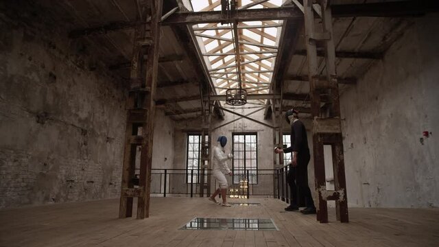Two fencers in white and black suits and masks compete with sabers in the old loft room where the dark side wins. The concept of the struggle between good and evil. Slow motion