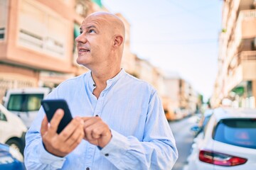 Middle age bald man smiling happy using smartphone at the city.