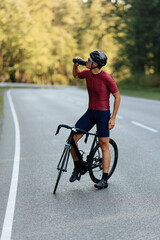 Strong man drinking water while standing on road with bike