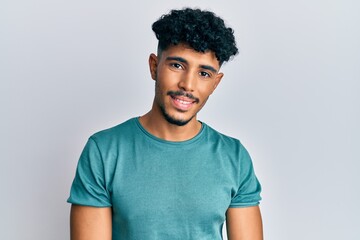Young arab handsome man wearing casual clothes looking positive and happy standing and smiling with...