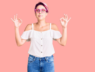 Obraz na płótnie Canvas Young beautiful woman with pink hair wearing casual clothes and glasses relax and smiling with eyes closed doing meditation gesture with fingers. yoga concept.