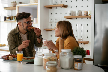 Young couple making sandwich at home. Loving couple drinking coffee while preparing the breakfast.