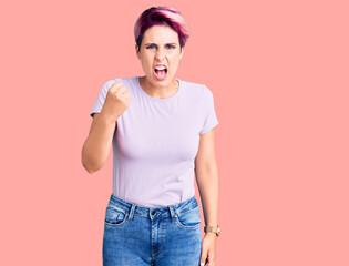 Young beautiful woman with pink hair wearing casual clothes angry and mad raising fist frustrated and furious while shouting with anger. rage and aggressive concept.