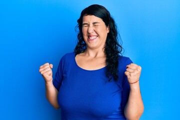 Plus size brunette woman wearing casual blue shirt excited for success with arms raised and eyes closed celebrating victory smiling. winner concept.