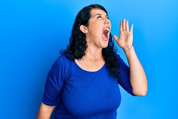 Plus size brunette woman wearing casual blue shirt shouting and screaming loud to side with hand on mouth. communication concept.