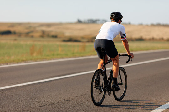 Back view of cyclist in helmet biking on asphalt road