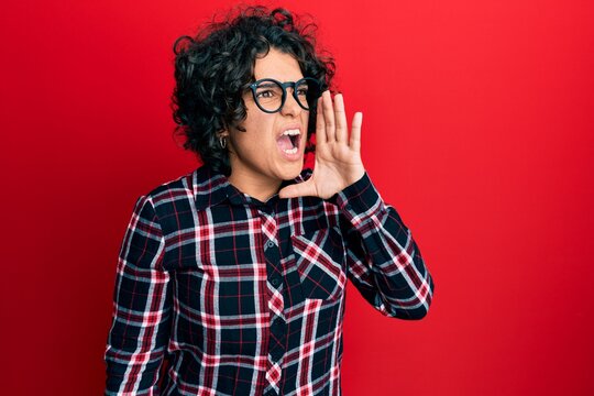 Hispanic woman with curly hair wearing casual clothes and glasses showing arms muscles smiling proud. fitness concept.