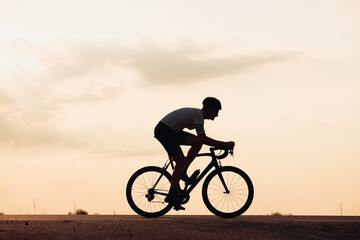 Fototapeta na wymiar Silhouette of man in helmet riding bike during sunset