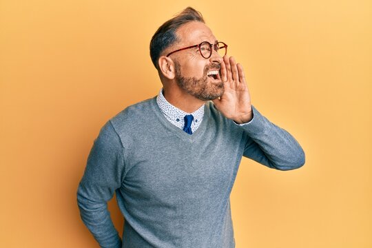 Handsome middle age man wearing glasses shouting and screaming loud to side with hand on mouth. communication concept.