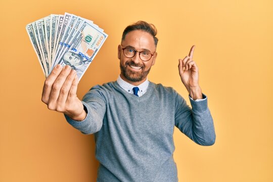 Handsome middle age man holding dollars smiling happy pointing with hand and finger to the side