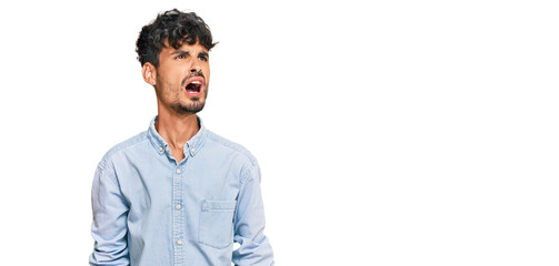 Fototapeta premium Young hispanic man wearing casual clothes angry and mad screaming frustrated and furious, shouting with anger. rage and aggressive concept.