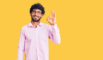 Handsome young man with curly hair and bear wearing business clothes smiling positive doing ok sign with hand and fingers. successful expression.