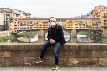 Coronavirus and Christmas mood in Europe. man in protective medical mask and Santa hat in historic center of Florence Italy. Covid-19 quarantine in Europe  Italy, France, Germany, Spain