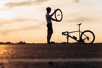 Active man in silhouette repairing bike on road