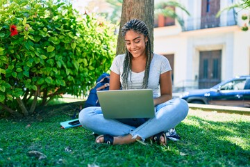 Young african american student woman smiling happy using computer laptop sitting on the grass at the university campus