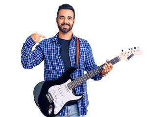 Young hispanic man playing electric guitar pointing finger to one self smiling happy and proud