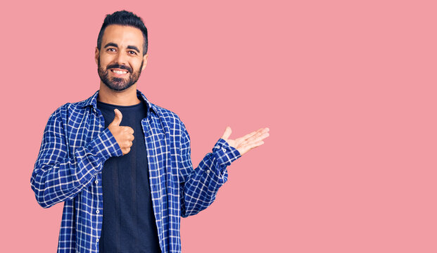 Young hispanic man wearing casual clothes showing palm hand and doing ok gesture with thumbs up, smiling happy and cheerful