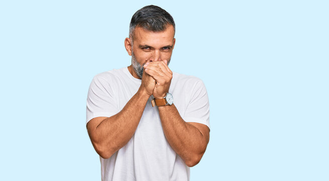 Middle age handsome man wearing casual white tshirt laughing nervous and excited with hands on chin looking to the side